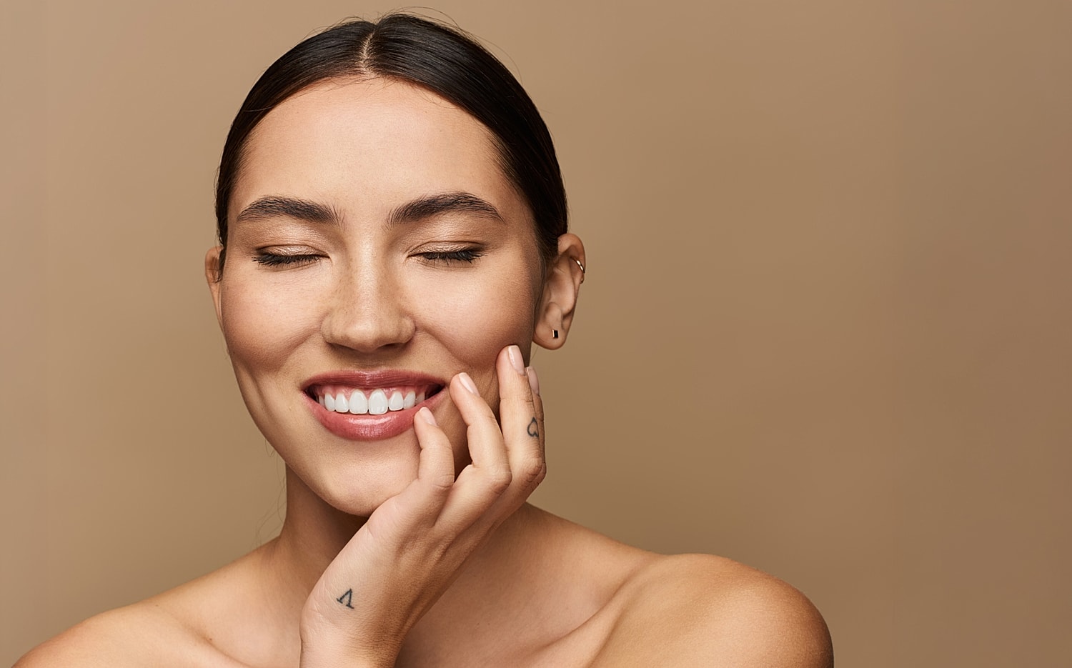 Smiling woman with closed eyes, neutral background.