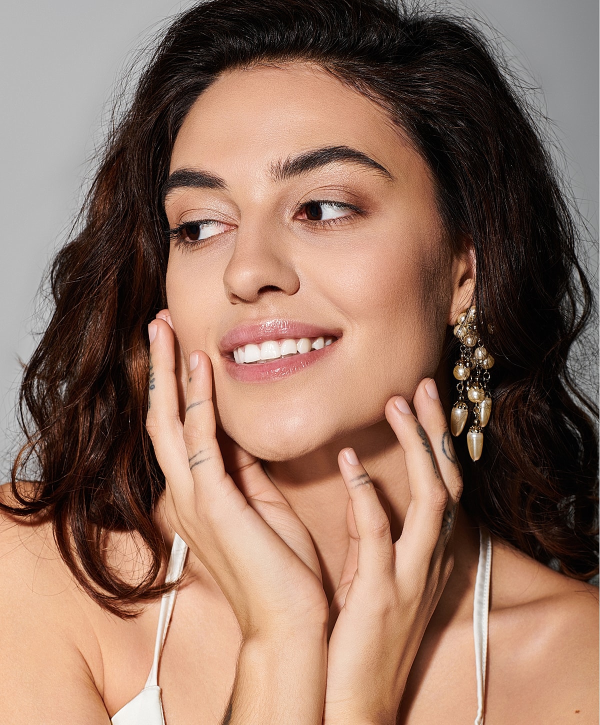 Smiling woman with earrings touching her face.