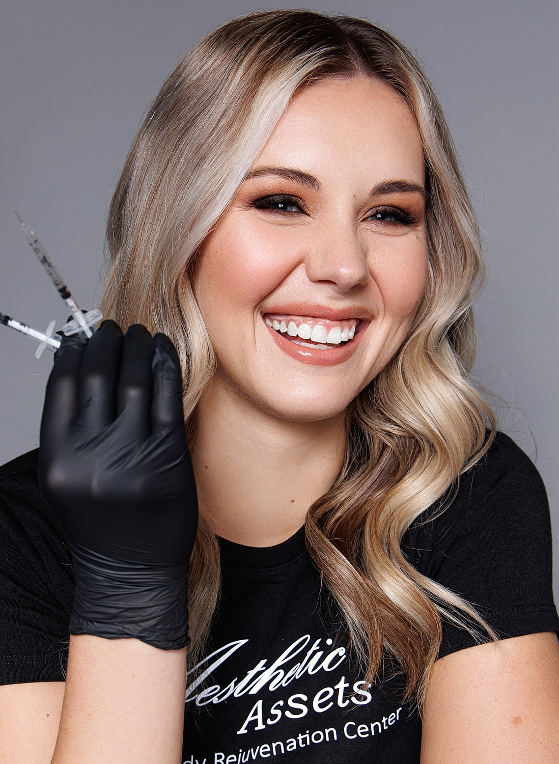 Smiling woman holding syringes for aesthetic treatments.