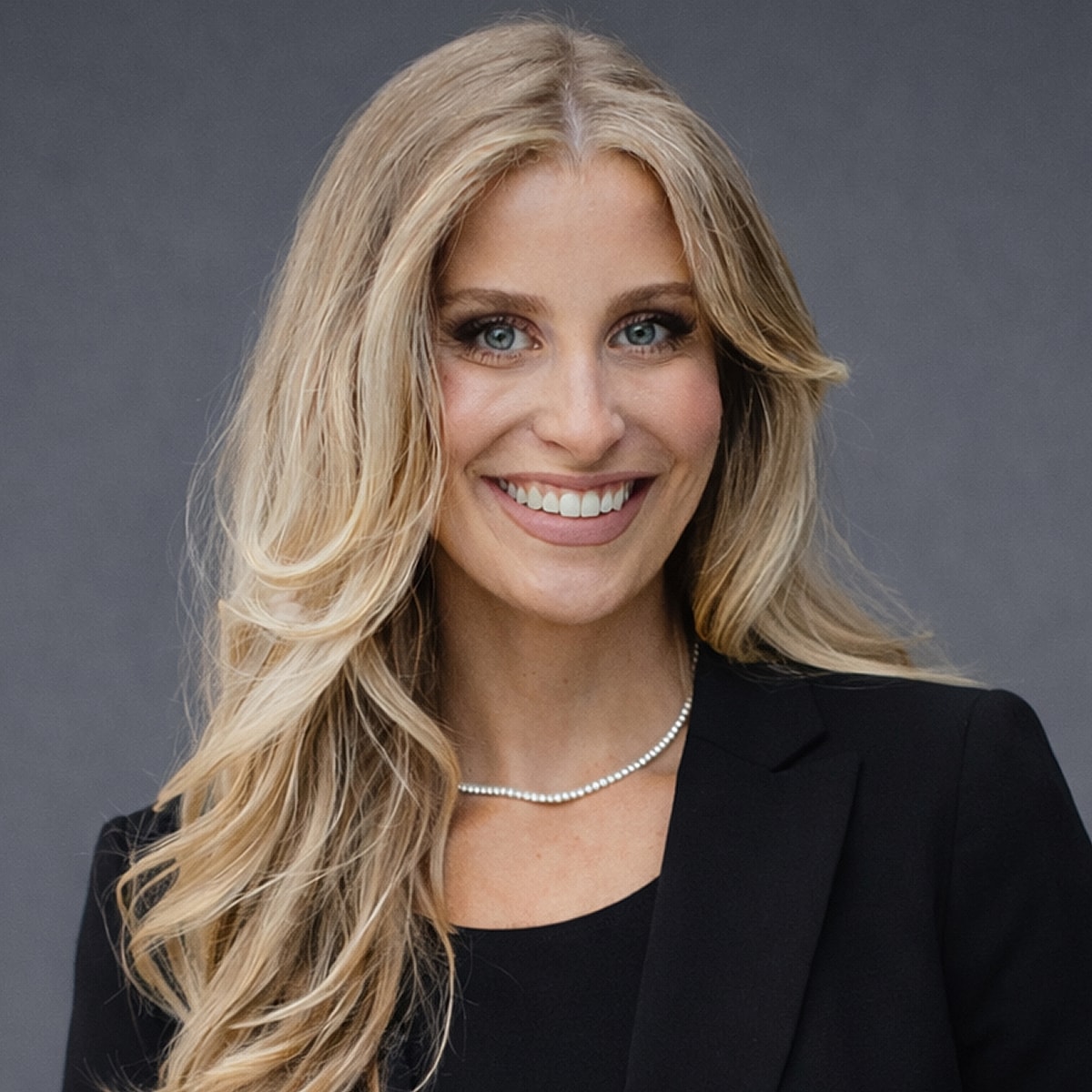 Smiling woman in professional attire with necklace.