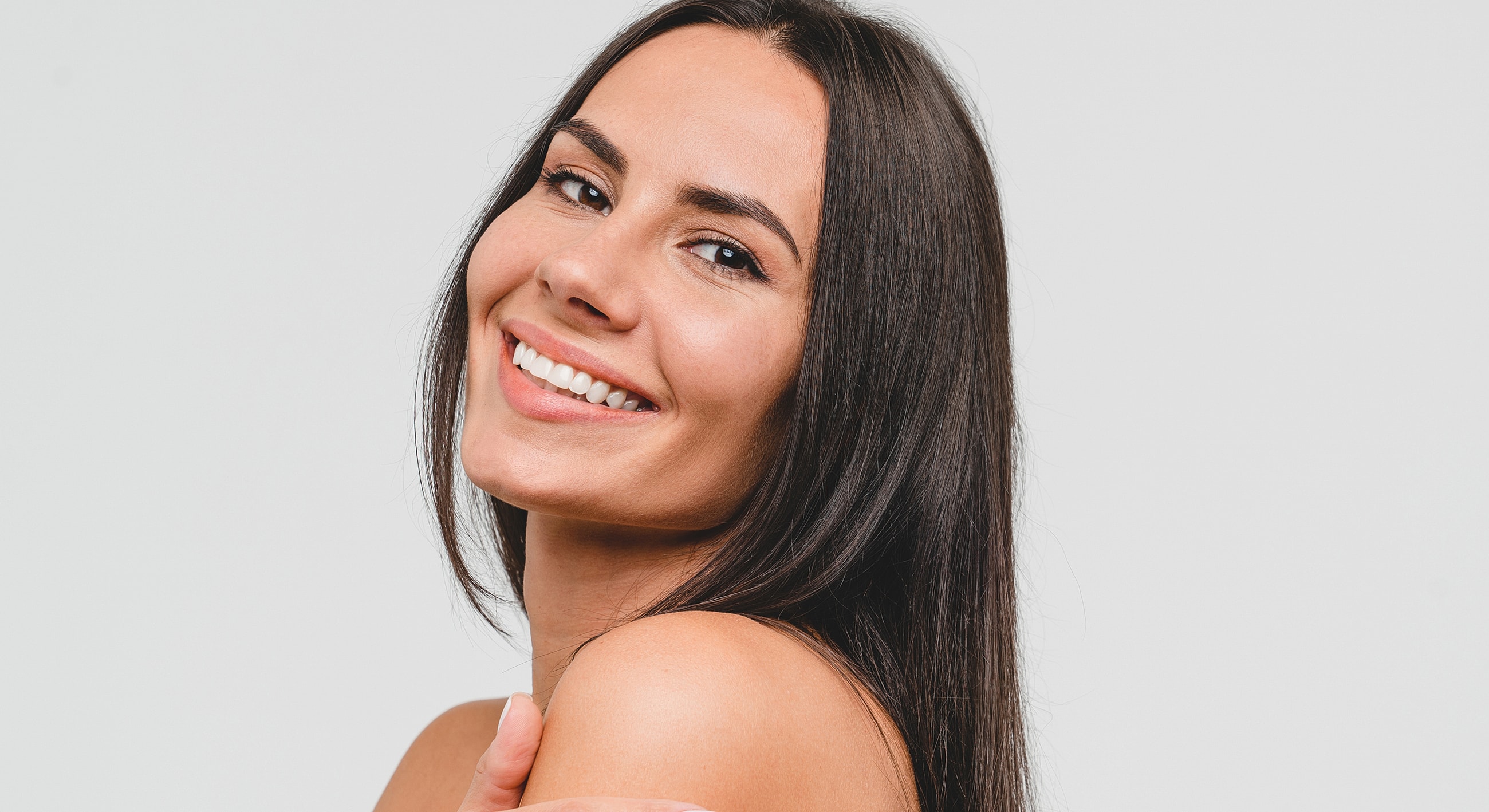 Smiling woman with long dark hair, gray background.